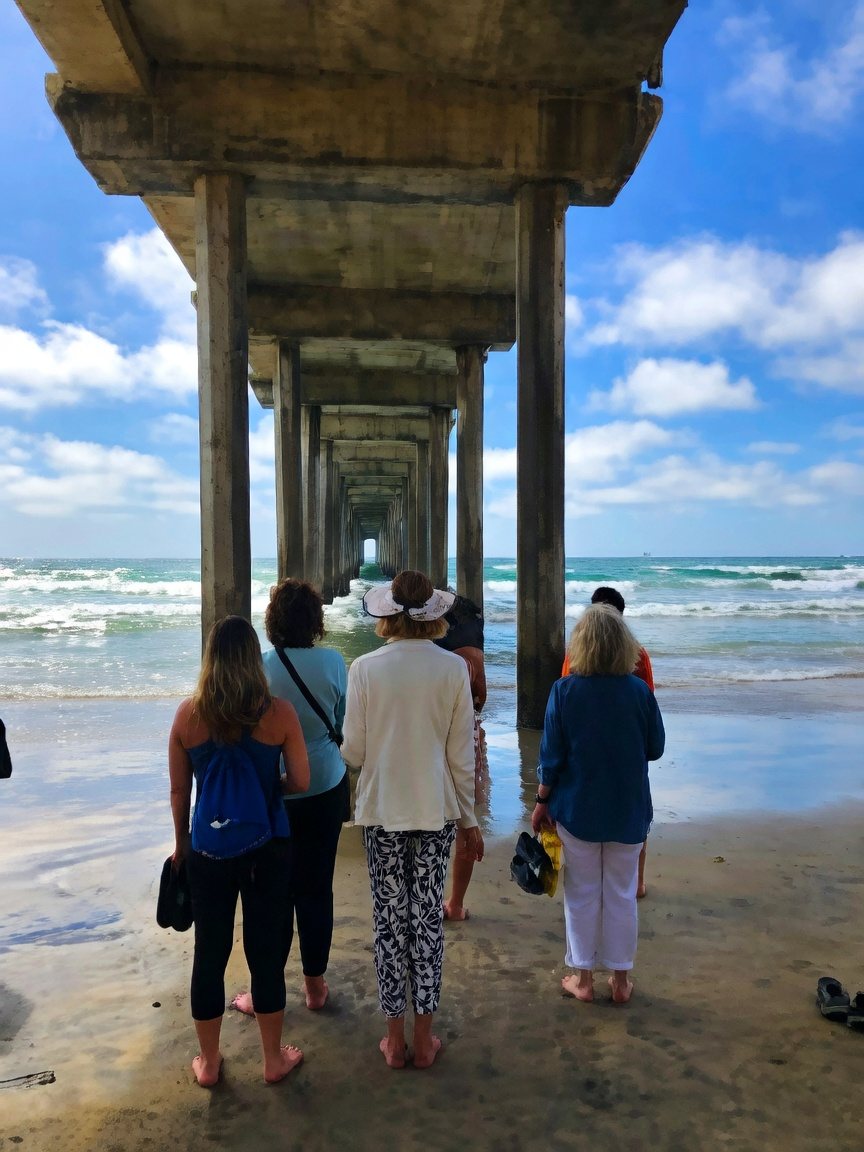 Retreat students standing barefoot under Scripps Pier at La Jolla, gazing toward the horizon